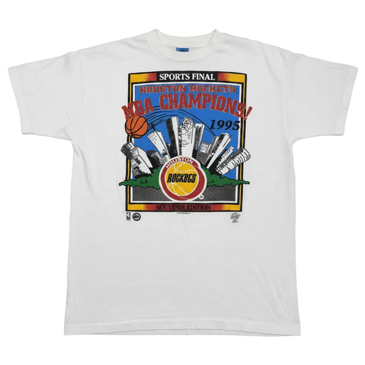 A white short-sleeve t-shirt with a vintage 1995 Houston Rockets NBA Champions graphic print on the front, No back hit.  This shirt has small hole on the left shoulder about the size of a dime.
